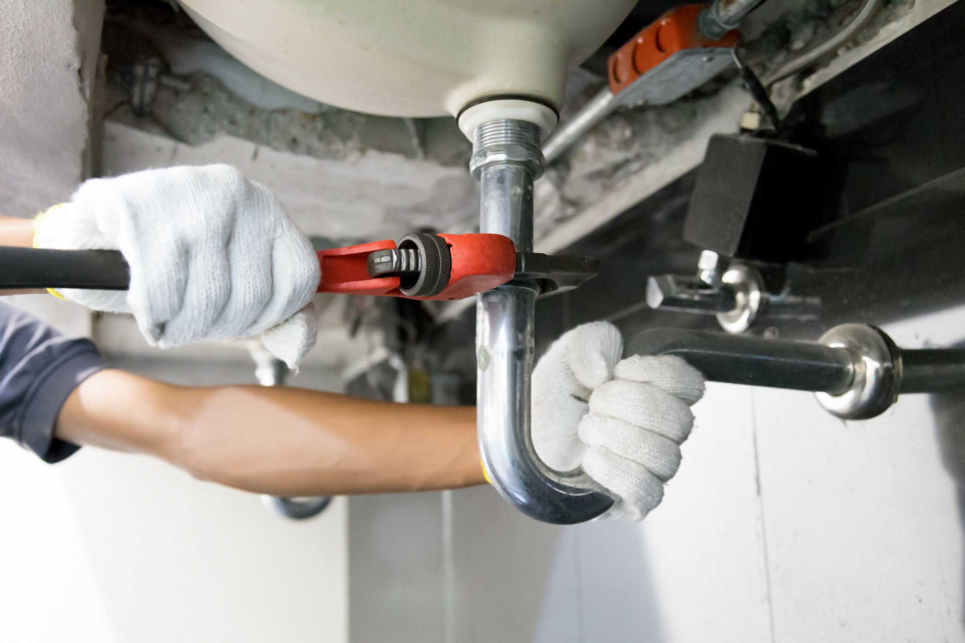Technician plumber using a wrench to repair a water pipe under the sink. Concept of maintenance, fix water plumbing leaks, replace the kitchen sink drain, cleaning clogged pipes is dirty or rusty.