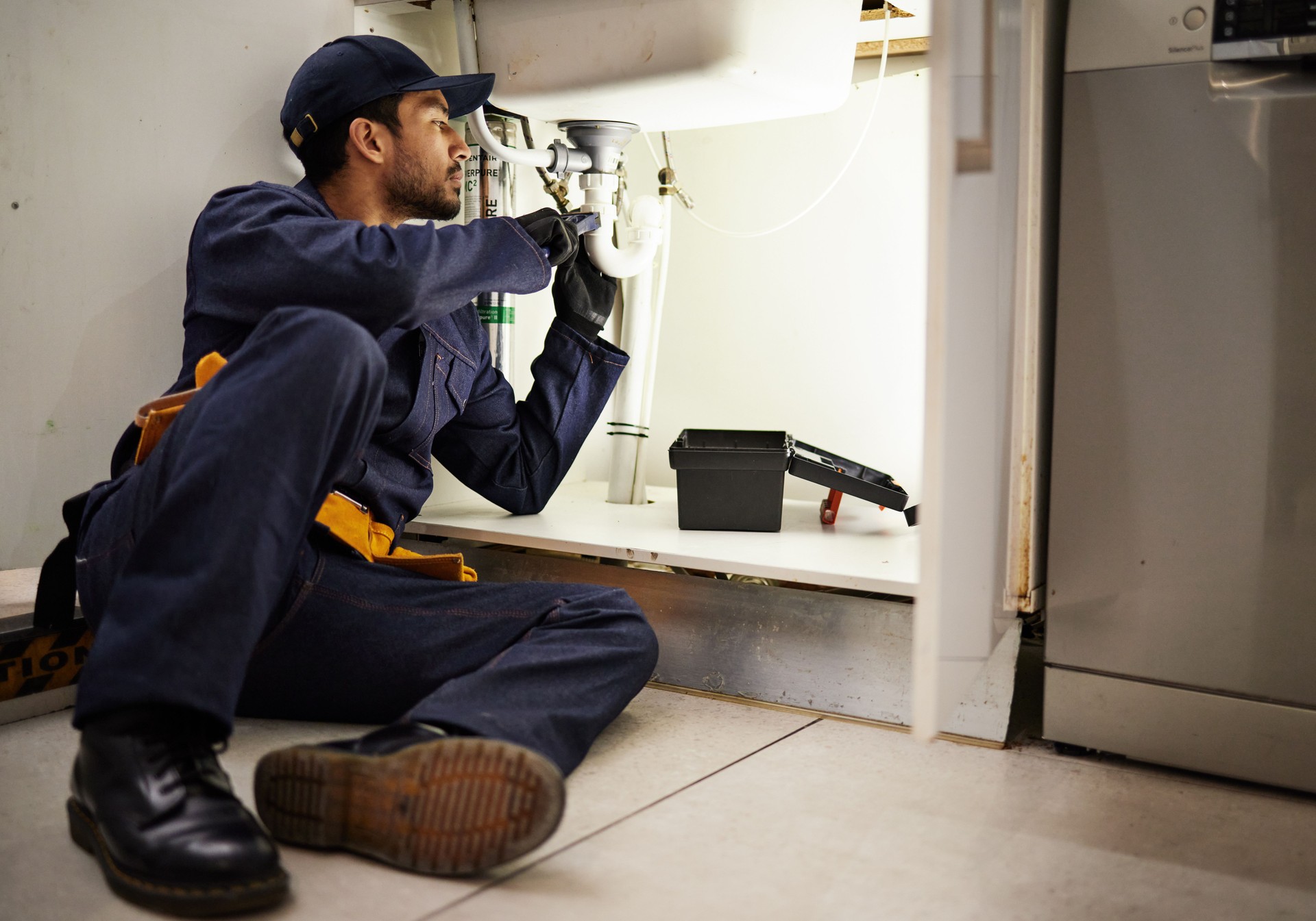 Plumbing, handyman and maintenance with man in kitchen for repair, industrial and inspection. Pipes, tools and safety with male plumber fixing sink for home improvement, drainage and water system